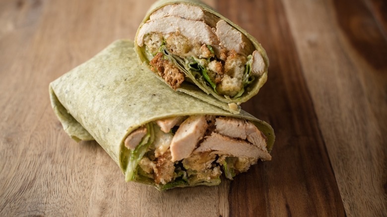 chicken caesar wrap cut in half on wooden surface