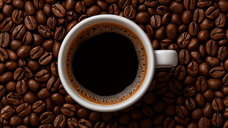 White cup of black coffee surrounded by coffee beans