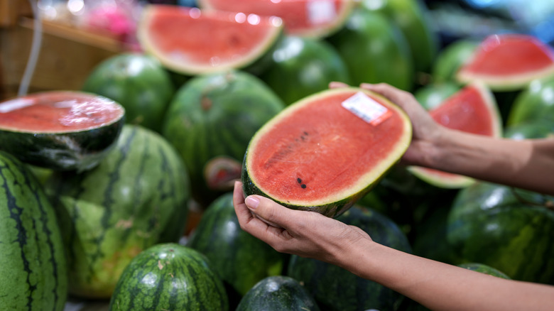 Someone picking out a wrapped half watermelon in a supermarket