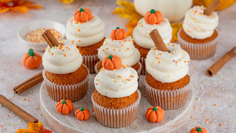 pumpkin spice cupcakes on tray decorated with fondant pumpkins.