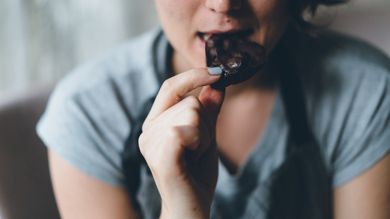 A person with painted nail eats a piece of chocolate