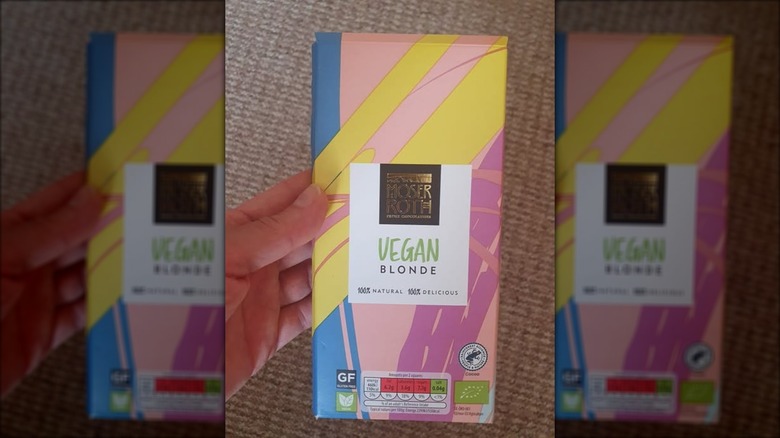 A hand holds a discontinued Moser Roth Vegan Blonde chocolate bar