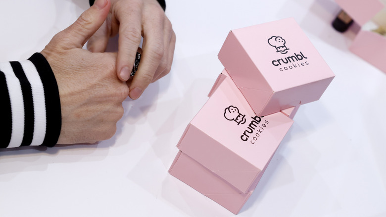 hands clasped in front of pink crumbl cookie boxes