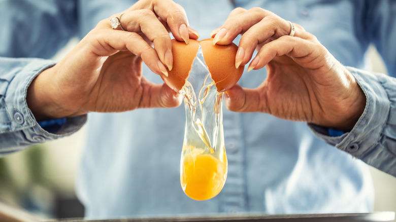 Hands crack a brown egg