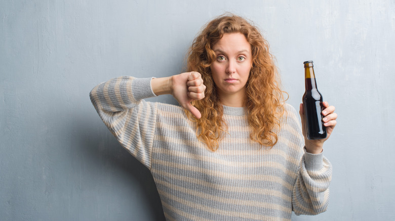 A woman holding a beer gives a thumbs-down