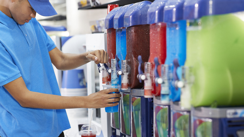 A young man filling up a slushy from a slushy machine
