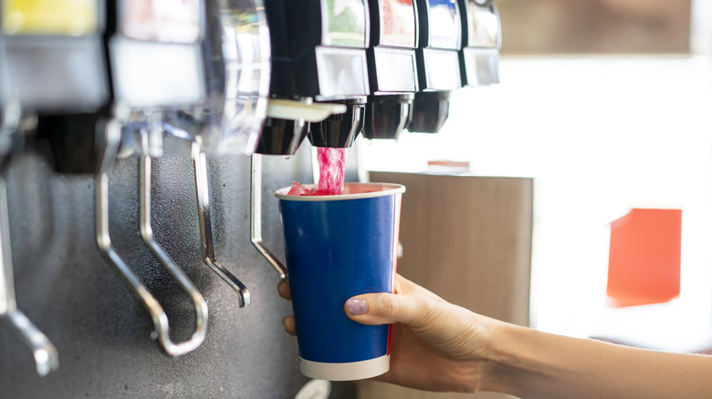 Someone filling a soda cup at a restaurant soda fountain machine