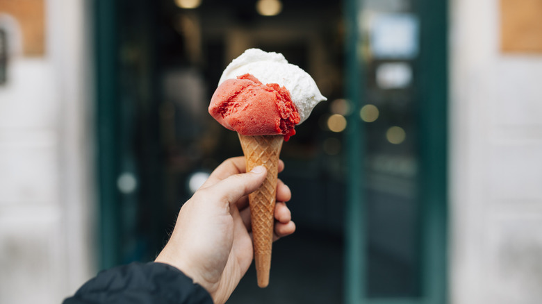 holding waffle cone containing red and white gelato