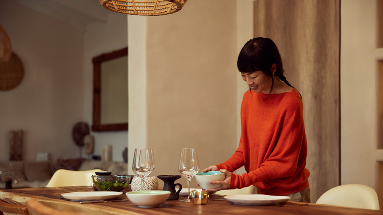 Smiling woman setting dinner table at home.