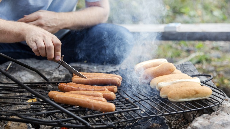person grills hot dogs on makeshift outdoor grill