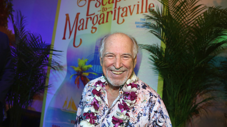 Jimmy Buffett smiling before poster of musical "Escape To Margaritaville"