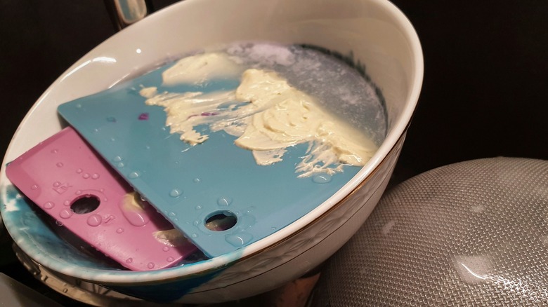 Kitchen equipment with butter on it soaking in bowl of water
