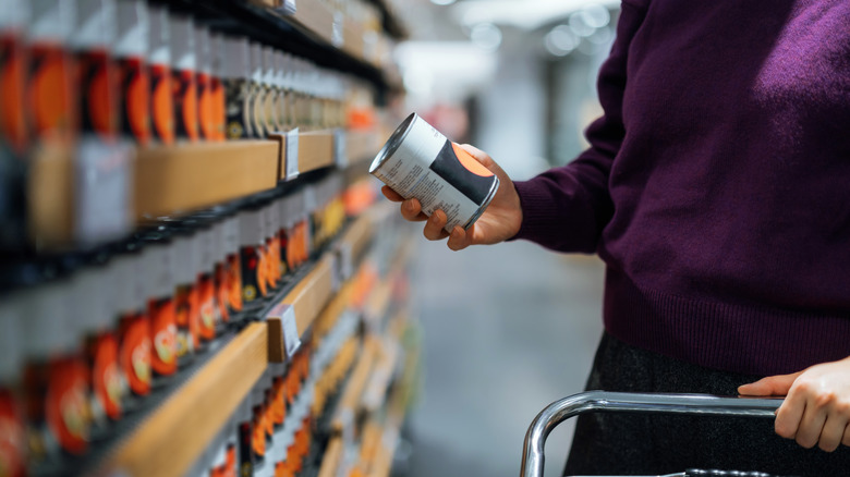 Cropped shot of person with grocery cart looking at can in aisle.