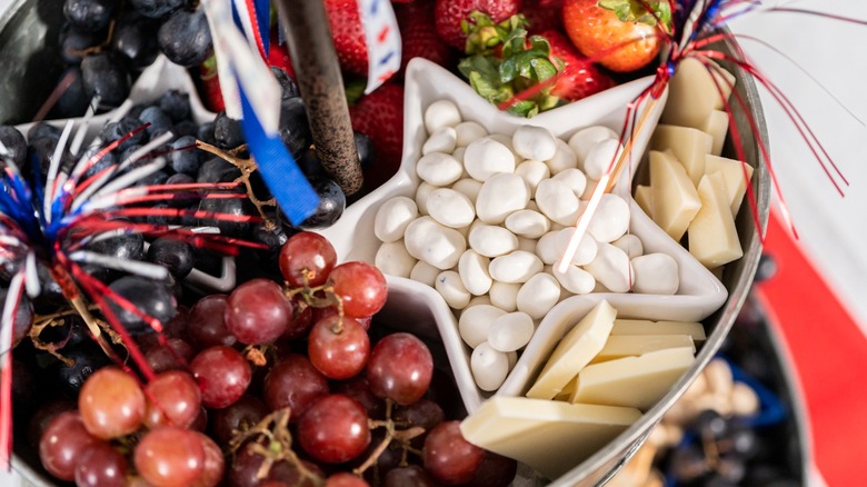 Yogurt-coated nuts in star-shaped container on charcuterie board with cheese and fruit