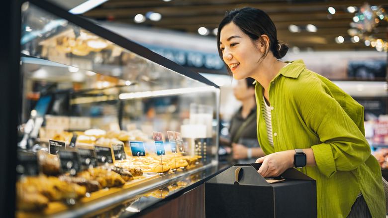 Woman holding box looks at pastry case.