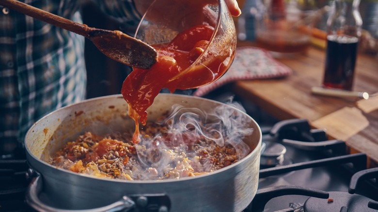 pouring tomatoes and tomato sauce into pasta dish