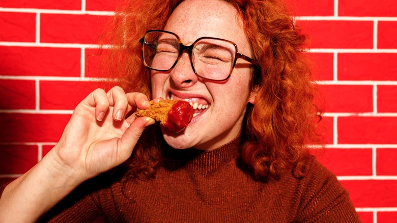 woman takes a bite of a chicken wing against red background