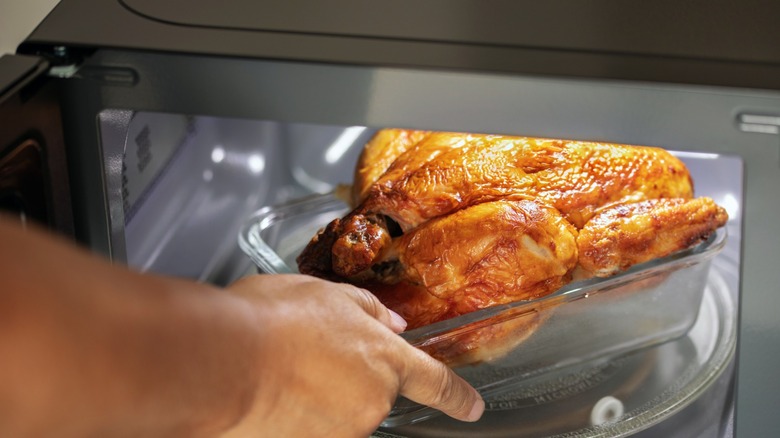 a hand places a whole chicken in a microwave
