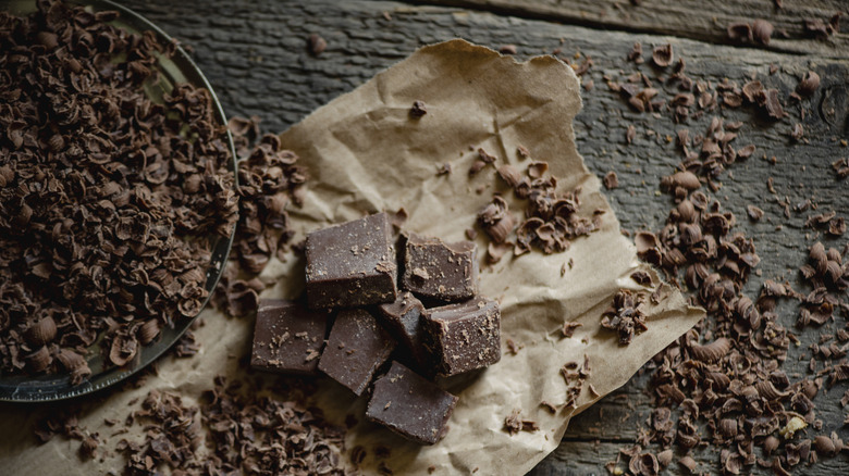 Chocolate shavings and broken chunks sit on against a rustic background
