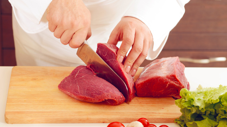 Knife slicing meat on a wooden cutting board