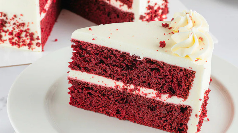 Slice of red velvet cake with whole cake in background