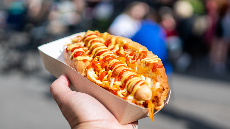 Hand holding hot dog in cardboard container.