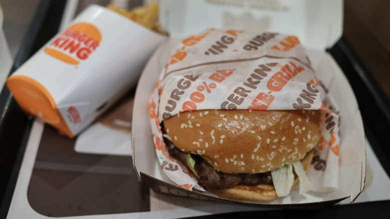 A Burger King Whopper in wrapper and takeout container with side of fries