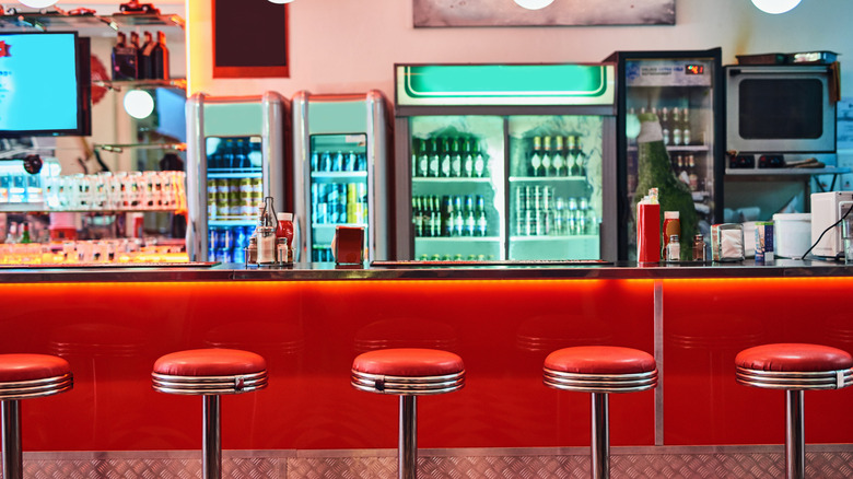 Vintage style diner interior with red stools at counter.