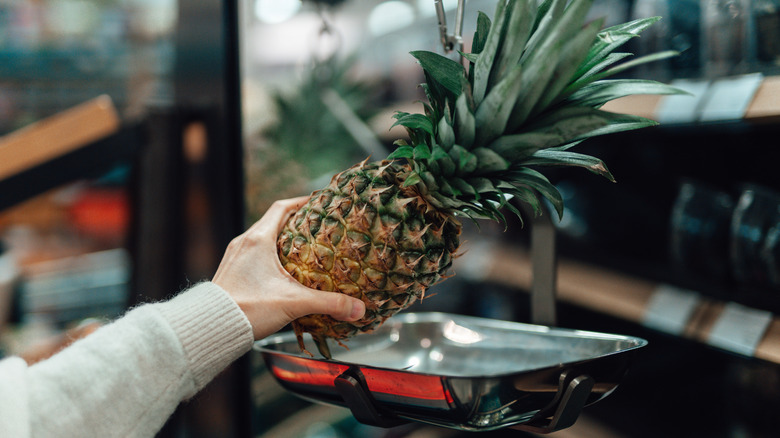 A close-up of someone weighing a pineapple at a grocery store
