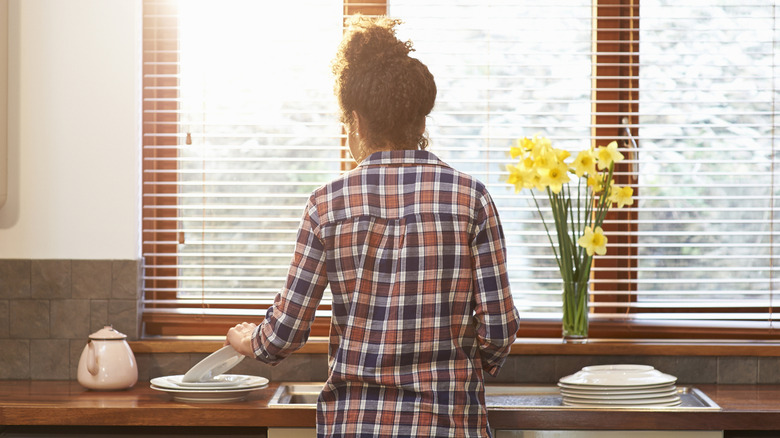 Person standing at kitchen sink, from behind.