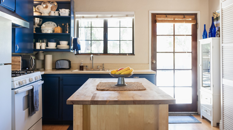 Wood-topped kitchen island in room with dark blue cabinets.