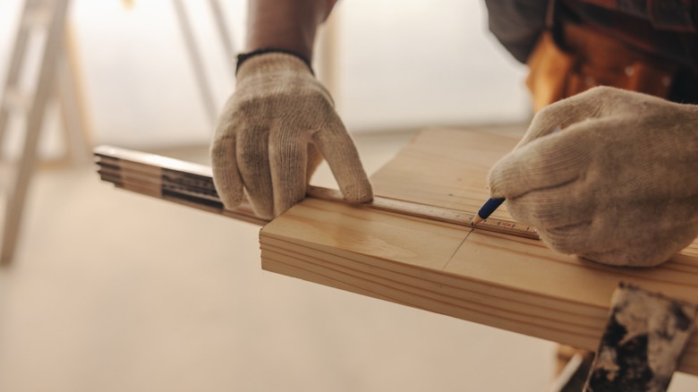 gloved hands measure a piece of wood before cutting
