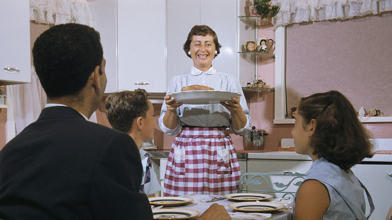 Mother brings dinner to table in 1960s picture.