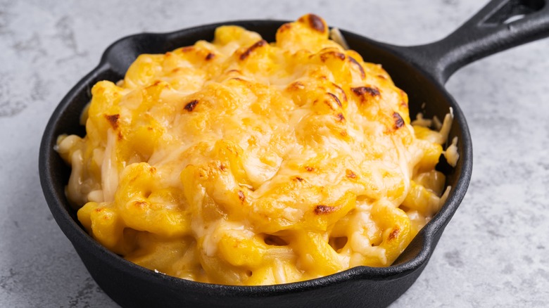A cast iron pan full of creamy mac and cheese with broiled cheese on top