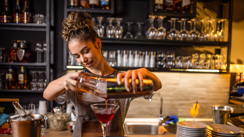 Female bartender pouring out a cocktail from a shaker
