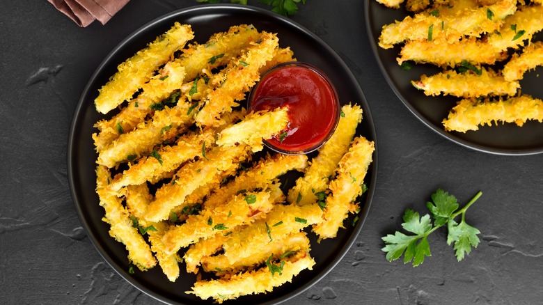 Zucchini fries on black plate with tomato based dipping sauce on the side