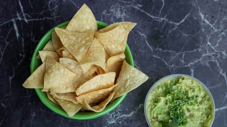 Bowl of tortilla chips beside bowl of guacamole on marble counter.