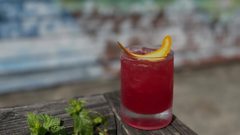 Red mixed drink in glass with orange twist closeup, blurred mural in background