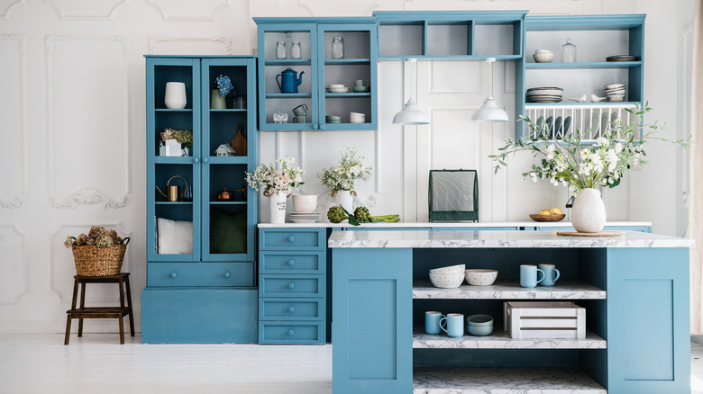 Kitchen with blue furniture and open cabinets containing many items.
