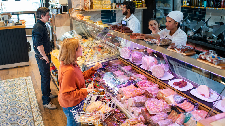 Customers at grocery deli case talking to workers.