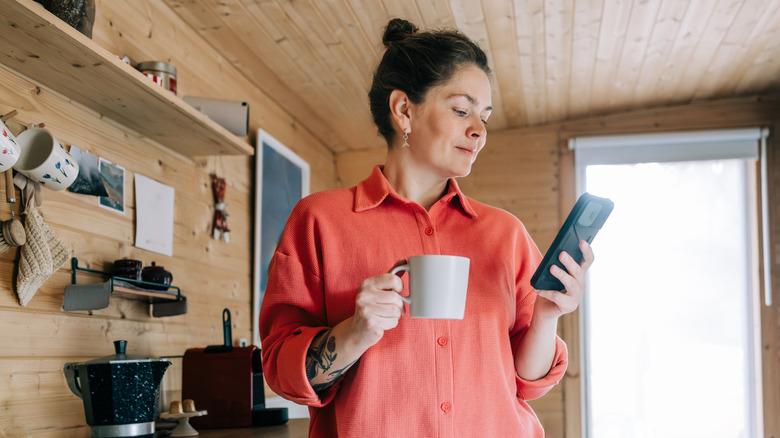 Woman checks phone in a kitchen with wood paneling.