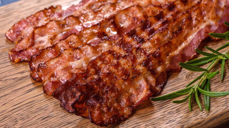 Cooked bacon on a wooden cutting board with rosemary to the side