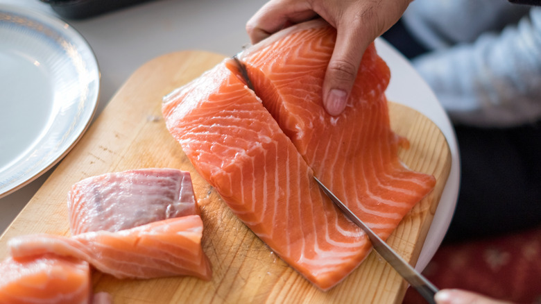 Someone slicing raw salmon on a chopping block