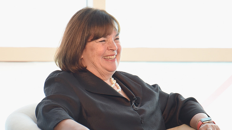 Ina Garten sitting in a white armchair smiling and laughing