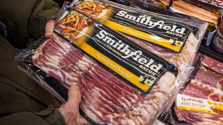 Person holding two packages of Smithfield bacon in grocery store