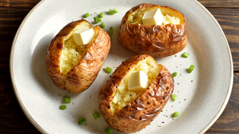 Three baked potatoes with butter and chives on white plate.
