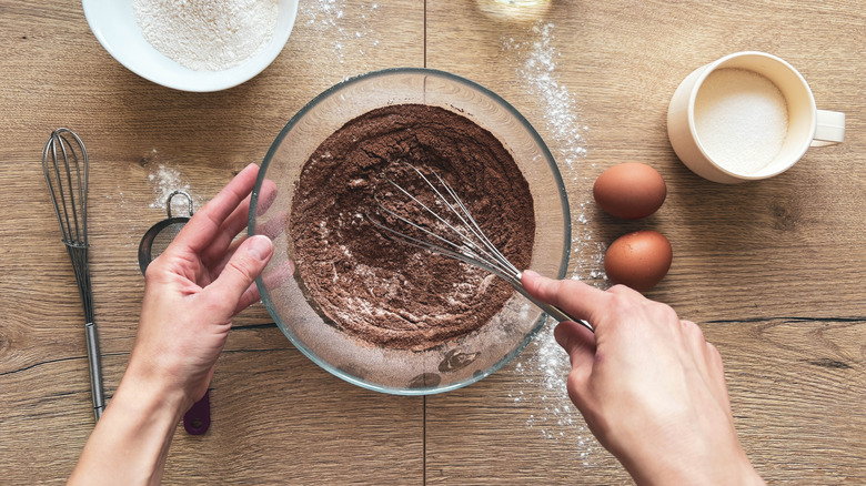 Overhead view of hands whisking dry cake ingredients in glass bowl.