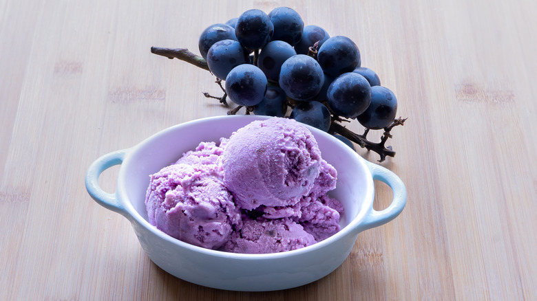 bowl filled with purple ice cream in front of grapes on vine