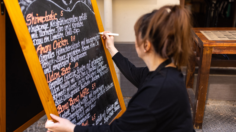 A woman writes on a restaurant menu board