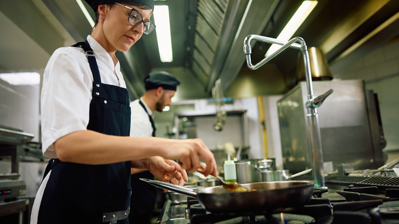 Chef in kitchen spooning sauce in pan.